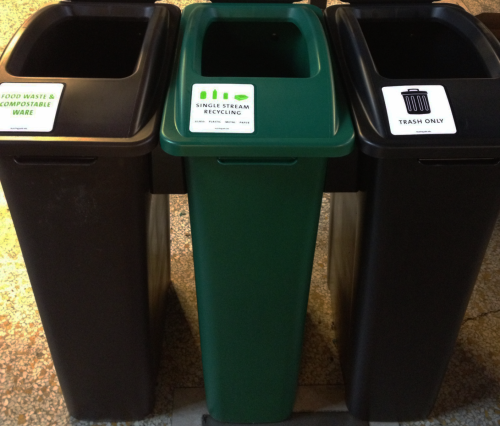 three plastic waste bins side-by-side. The bin on the left is brown and labeled &quot;Food waste and compostable ware.&quot; The center bin is green and labeled &quot;single stream recycling.&quot; The bin on the right is black and labeled &quot;trash only.&quot;