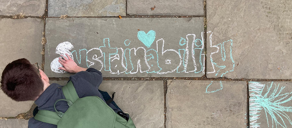 Overhead shot of student writing the word 'sustainability' in chalk on a bluestone walkway