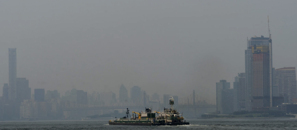 A ship in New York's East River with wildfire smoke enveloping skyscrapers in the background