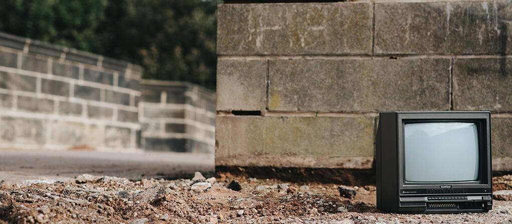 A photo of an old television by a concrete wall