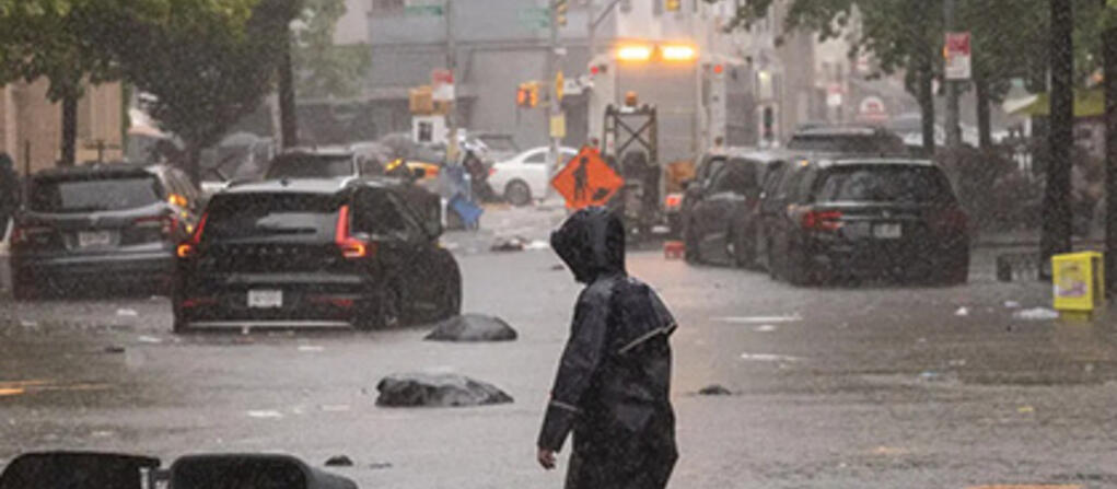 Person in raincoat wading through flooded streets in a U.S. city