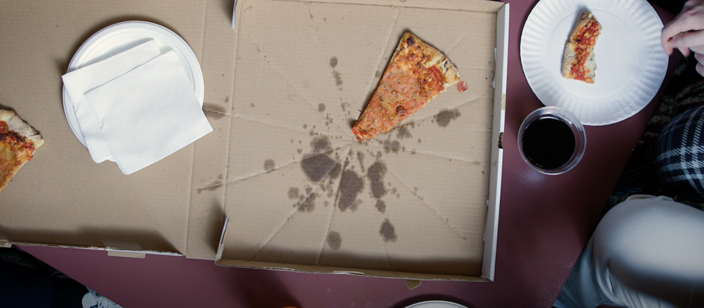 Overhead photo of a greasy pizza box and pizza slice