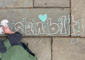 Overhead shot of student writing the word 'sustainability' in chalk on a bluestone walkway