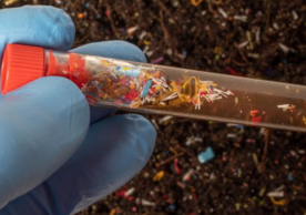 A gloved hand holding a vial of microplastics