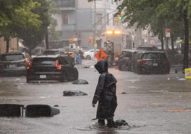 Person in raincoat wading through flooded streets in a U.S. city